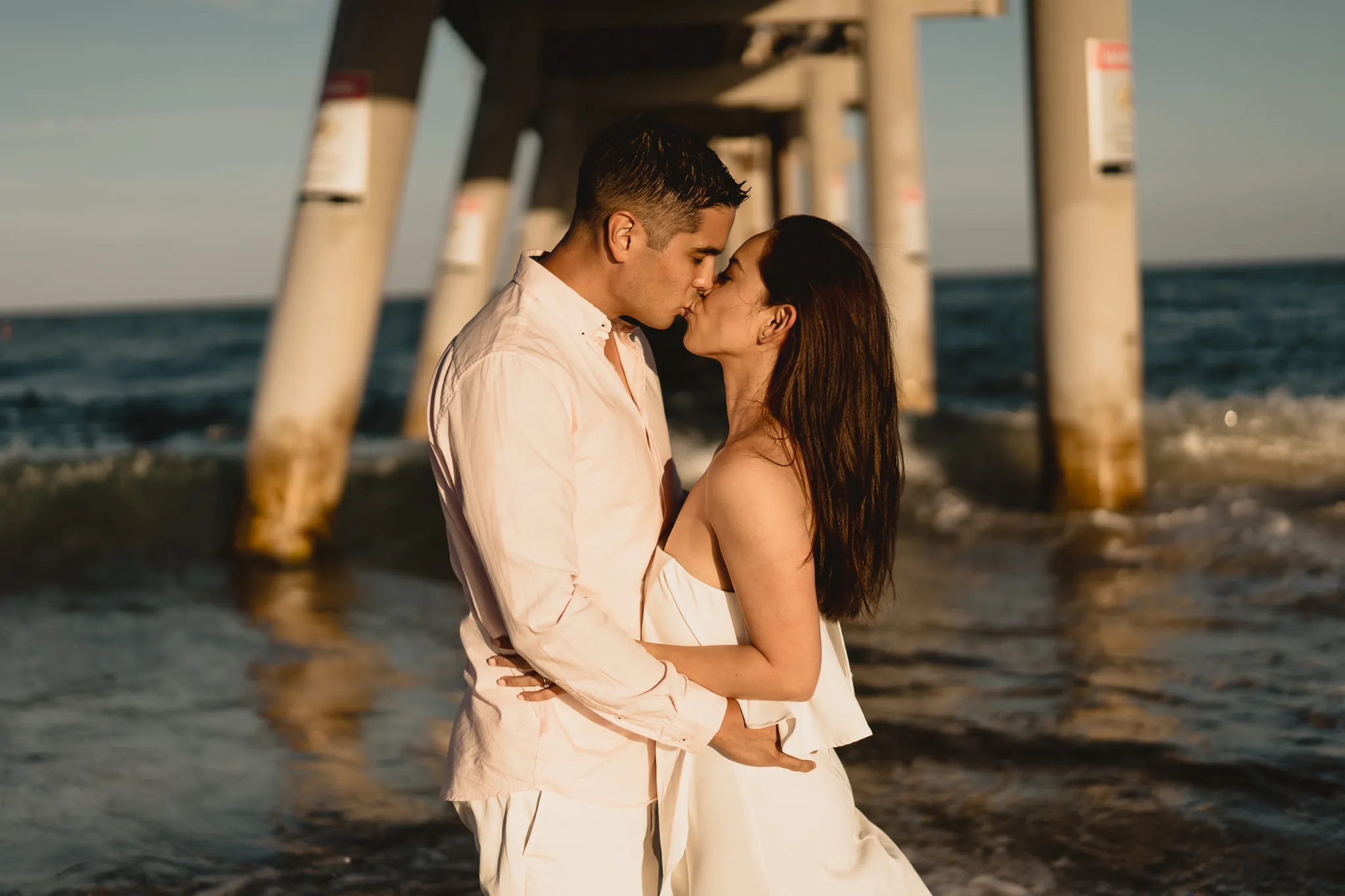 Rafaela and Mark kissing beneath the pier as the waves wash around the pylons